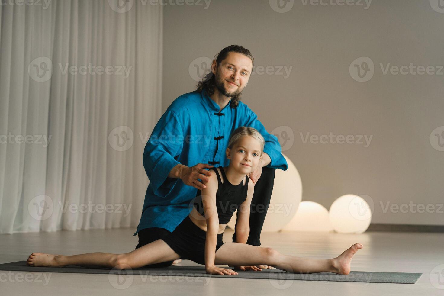 A yoga instructor in training helps a child to do exercises in the gym photo