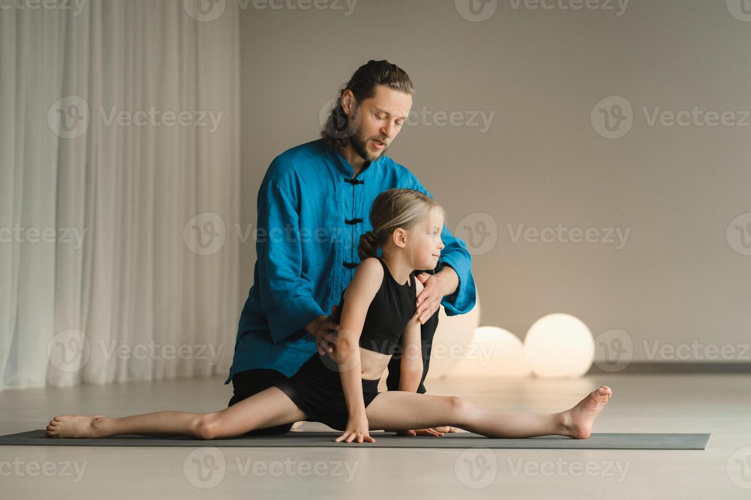 A yoga instructor in training helps a child to do exercises in the gym photo