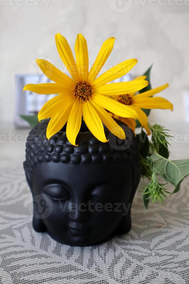 Black statuette of Buddha head with yellow flower. Harmony space. photo
