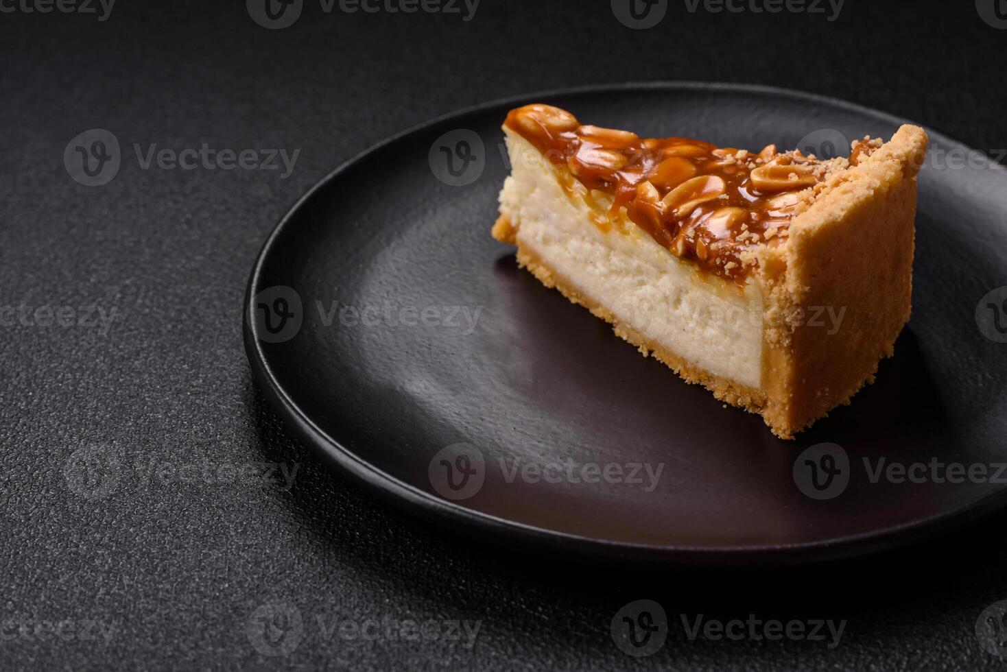 Delicious fresh cheesecake caramel peanut cake with cream and nuts on a ceramic plate on a dark concrete background photo