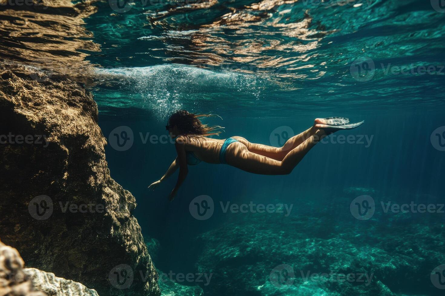 Woman swimming underwater near rocks in turquoise sea with flippers photo
