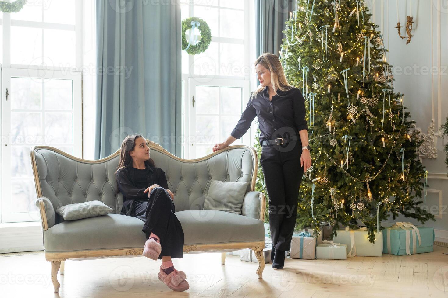 Happy Caucasian mother and her daughter are during Christmas, decorating a Christmas tree and having fun photo