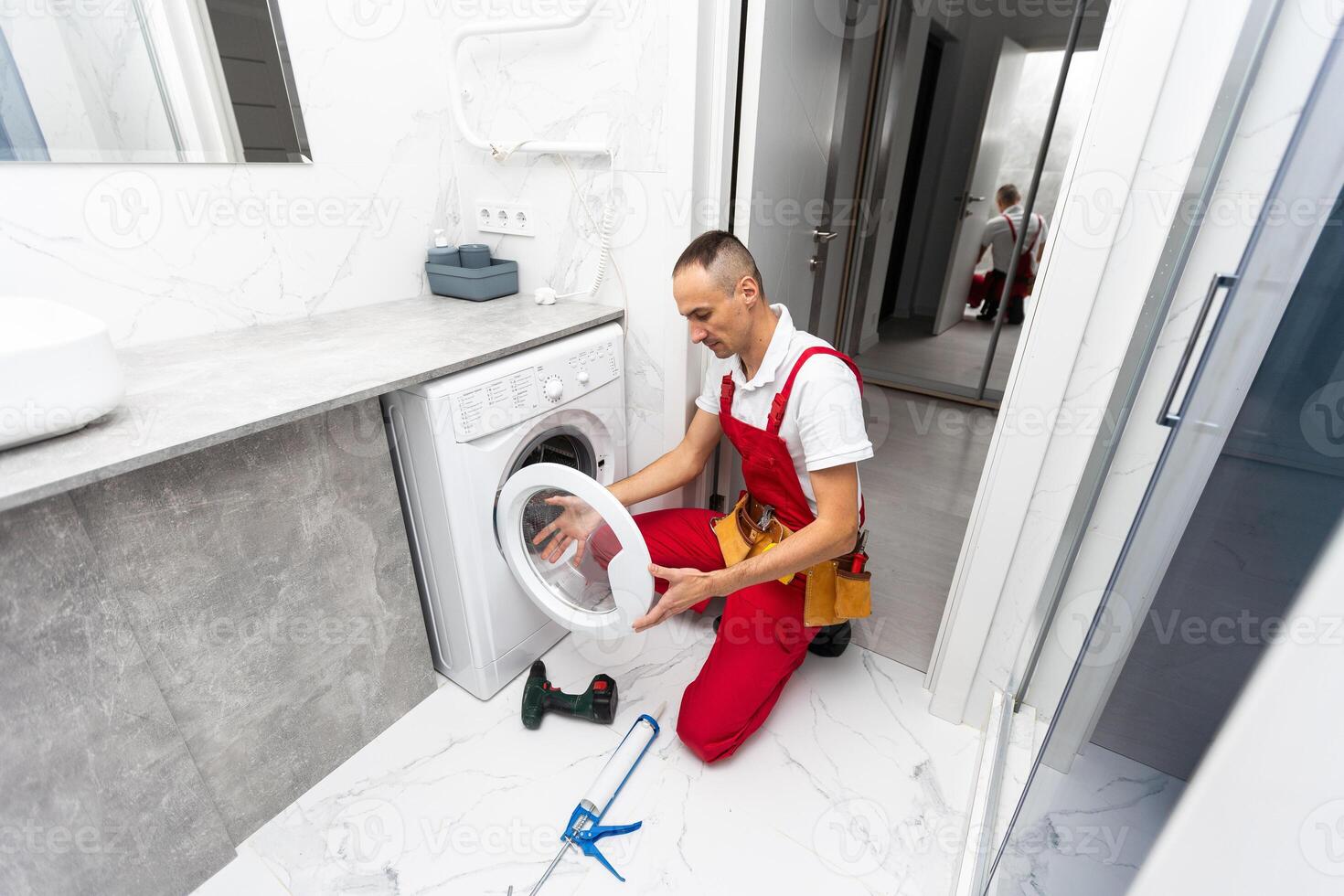 Professional mechanic repairing washing machine in domestic interior photo