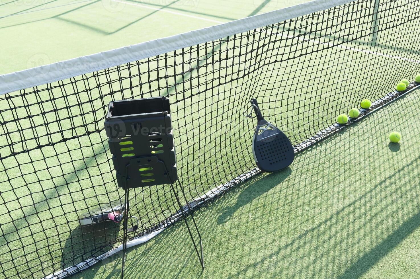 padel racket and yellow balls placed on court near net on sunny day photo