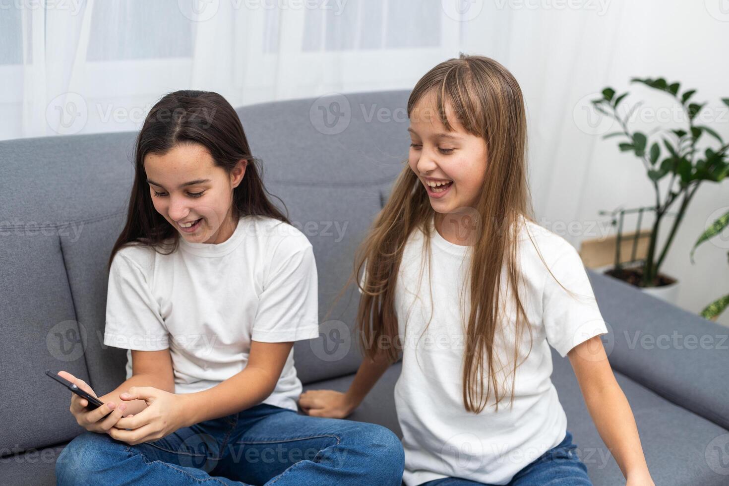 Child with smartphone at home. Two kids using smart phone, surfing internet or using social media. Two kids using online mobile phone, call, watching content, playing games, sitting on couch photo