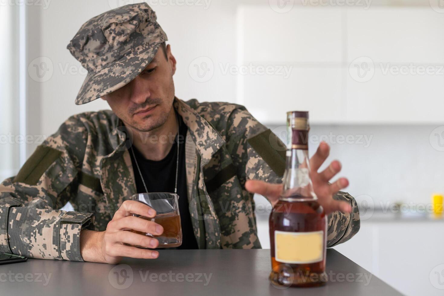 Depressed soldier with bottle sitting in living room. Alcohol addiction. photo