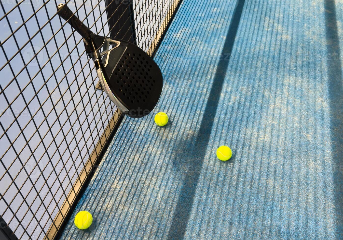 Padel racket and yellow ball behind net on a green court grass turf outdoors at sunset. Paddle is a racquet game. Professional sport concept with space for text photo