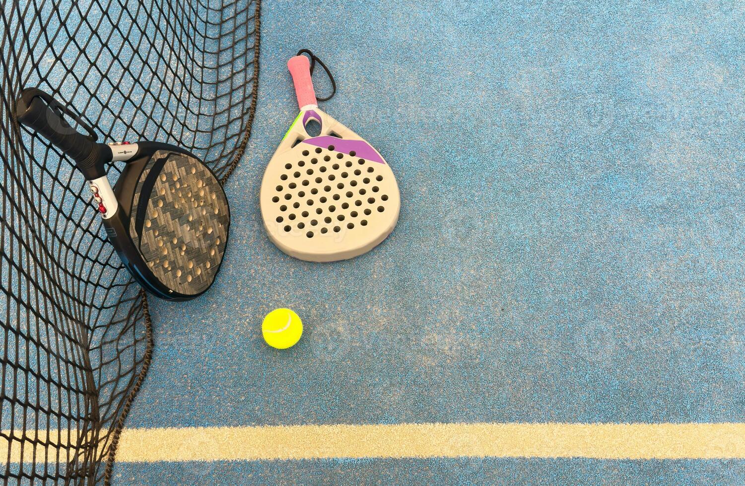 A padel tennis racket is laying on the ground next to a tennis ball on a padel court photo