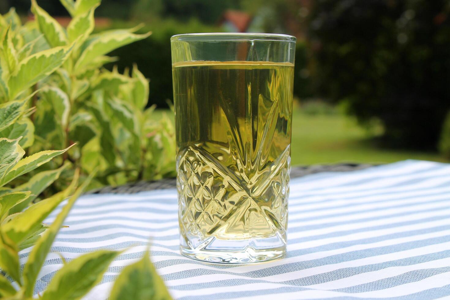 Clear drink in a tall glass on striped tablecloth in summer garden close-up. photo