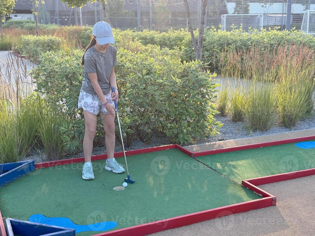 Little active child, cute toddler girl, playing miniature golf enjoying sunny summer vacation day outdoors in the park. photo