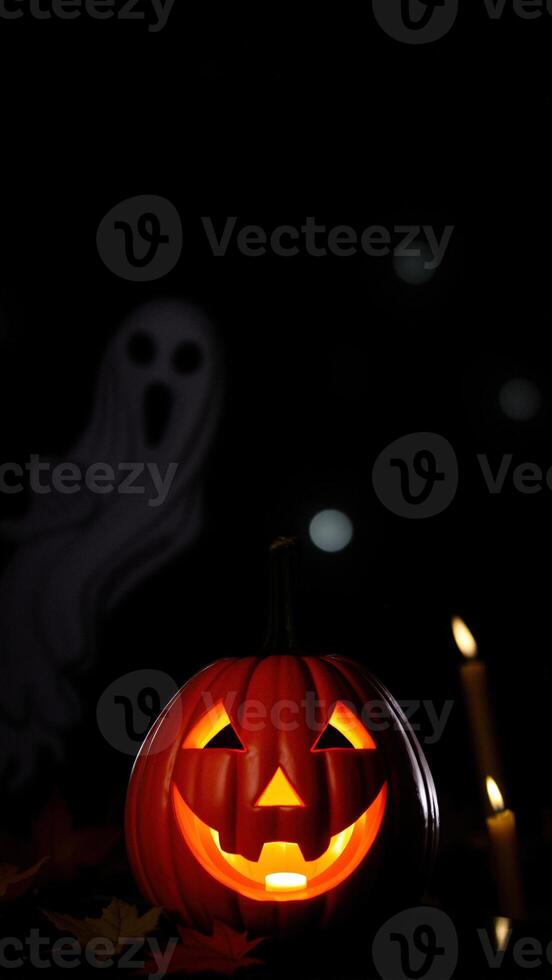Jack-o'-lantern glowing in the dark with ghost and candles photo
