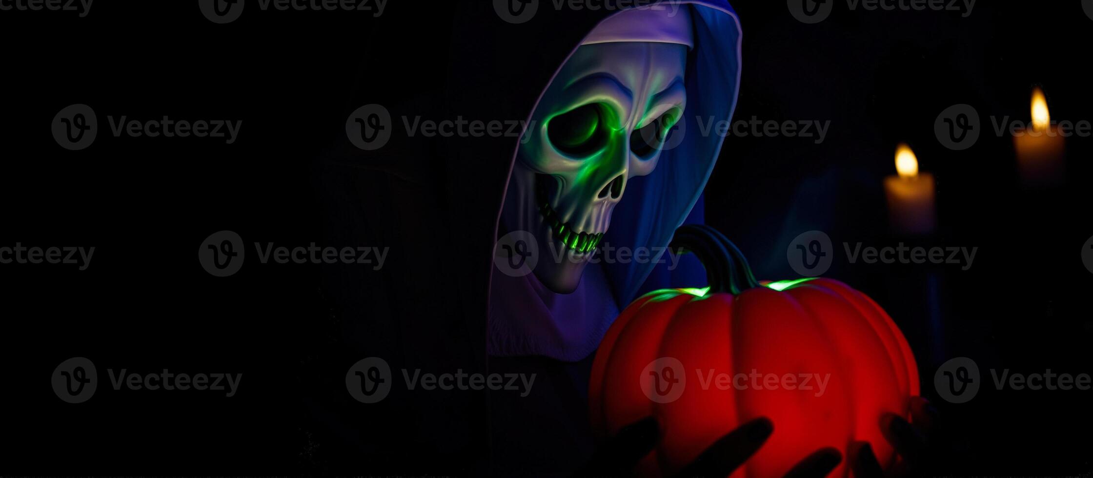 person wearing a skull mask holds a glowing red pumpkin photo