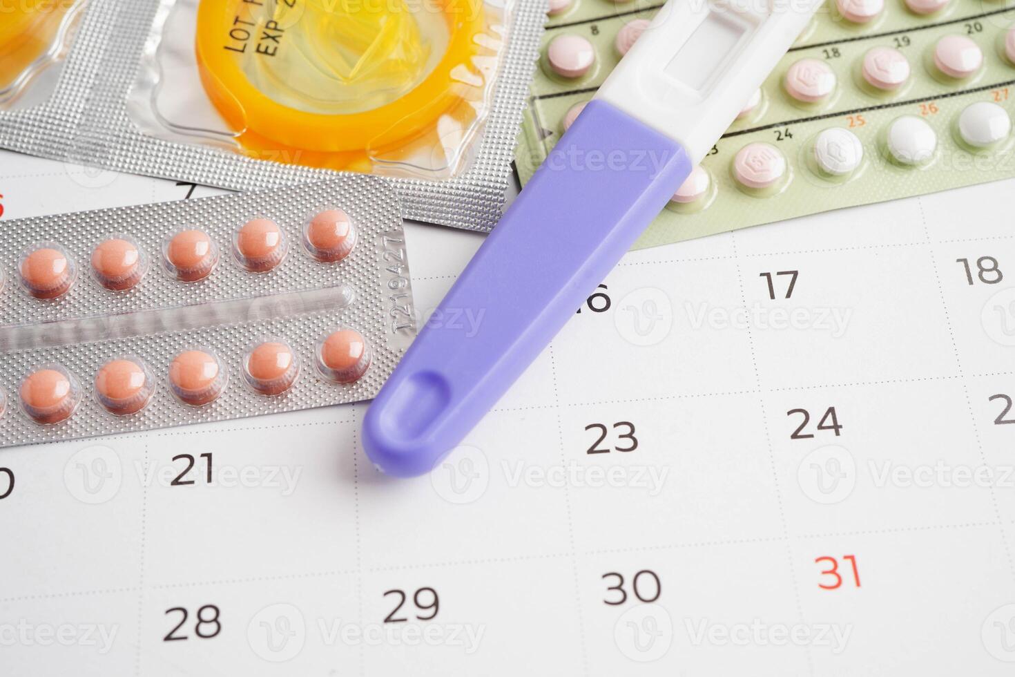 Pregnancy test with birth control pills and condom for female on calendar, ovulation day. photo