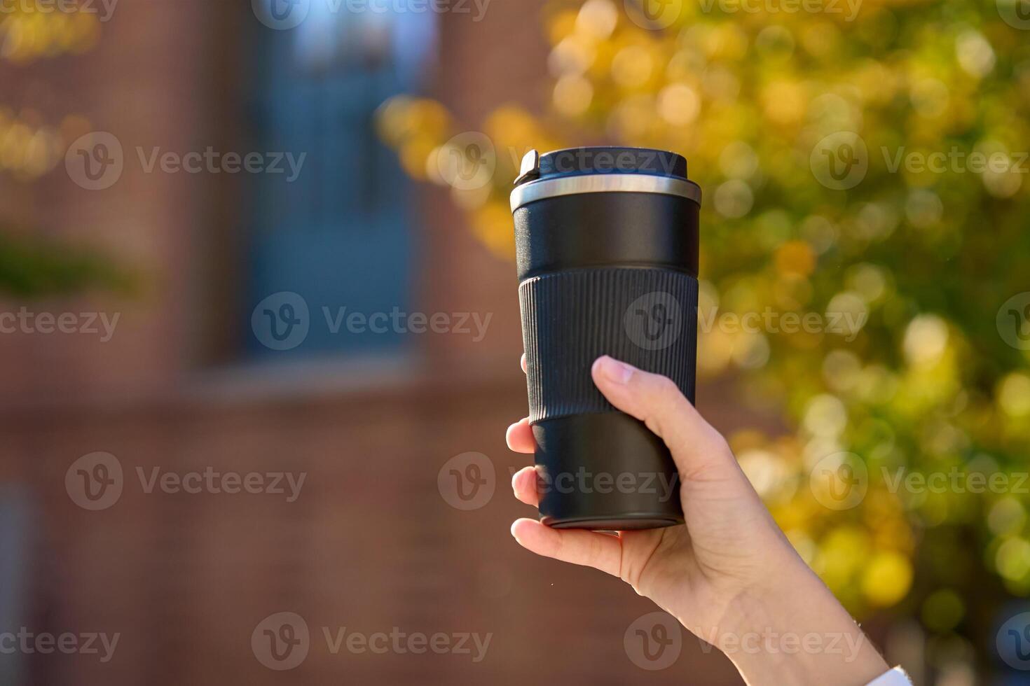 Woman holding reusable coffee cup on blurred autumn background. Concept of sustainable and eco-friendly living photo