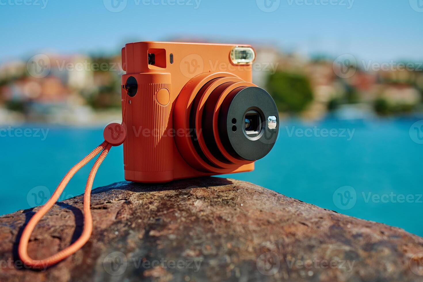 Orange instant camera on rock with seaside background photo