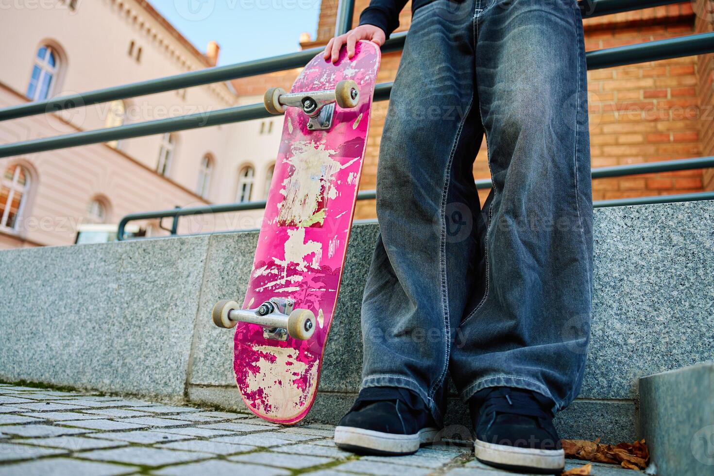 Skateboarder holding worn pink skateboard at street photo