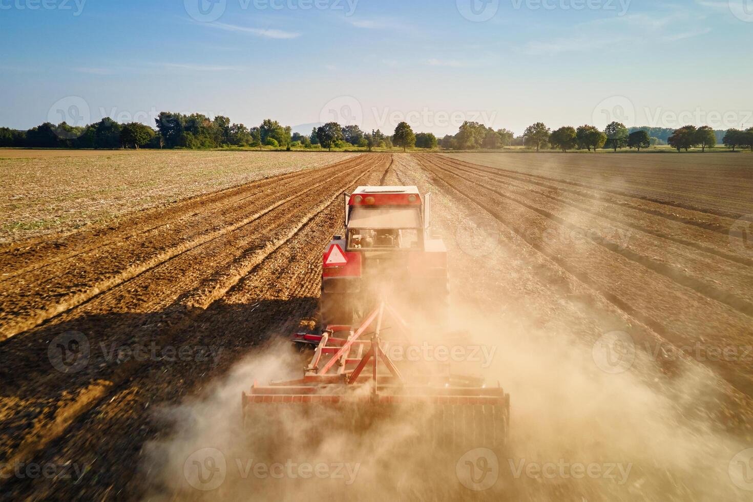 Tractor working in agricultural field, cultivating and plowing dry soil photo