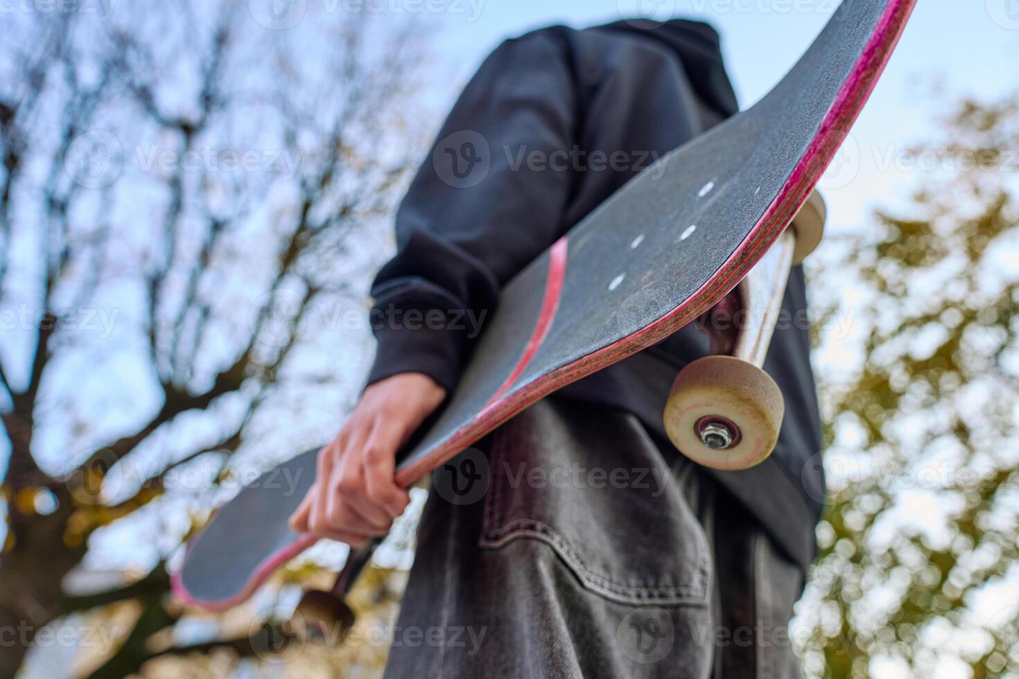 Skateboarder holding worn skateboard walks at street photo