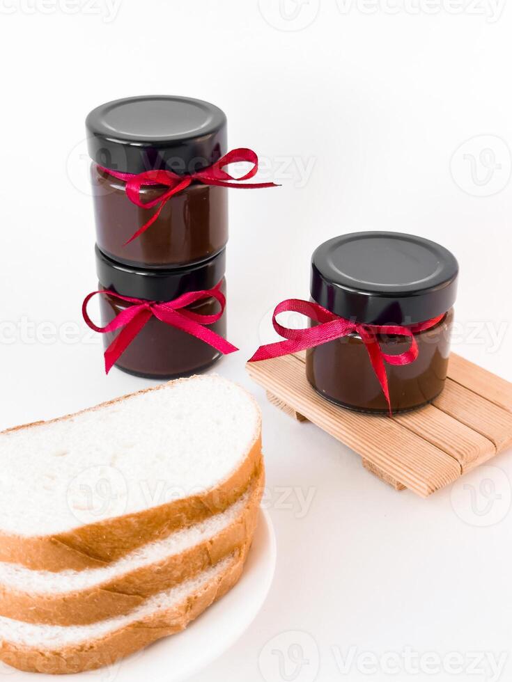 Homemade jam jars with red ribbons and bread slices on white background photo