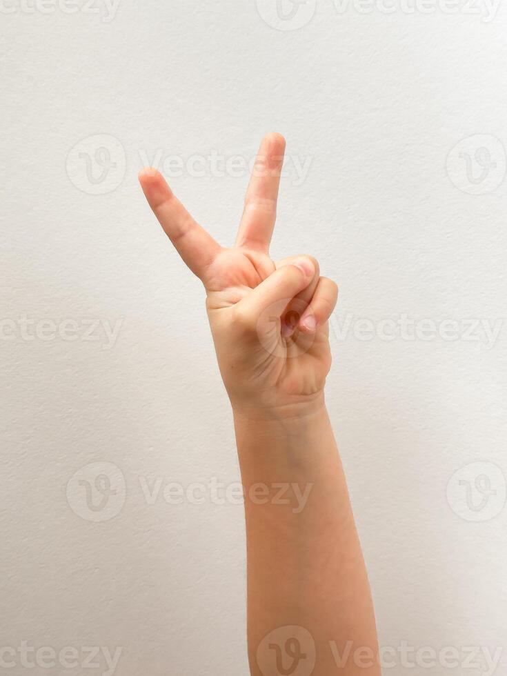 Peace gesture with childs hand on simple white background photo