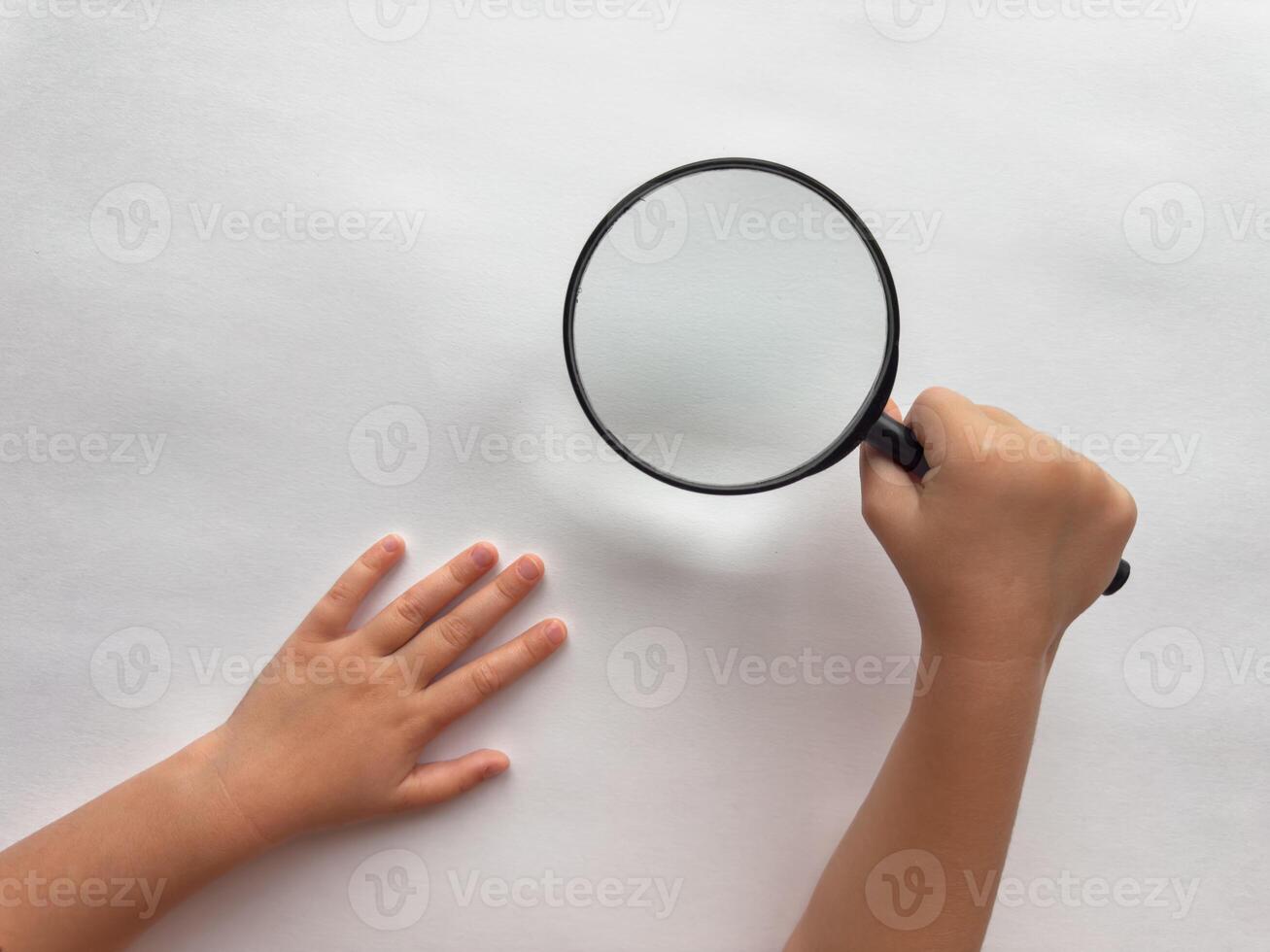 Childs curiosity. Hand holding magnifying glass over white surface photo