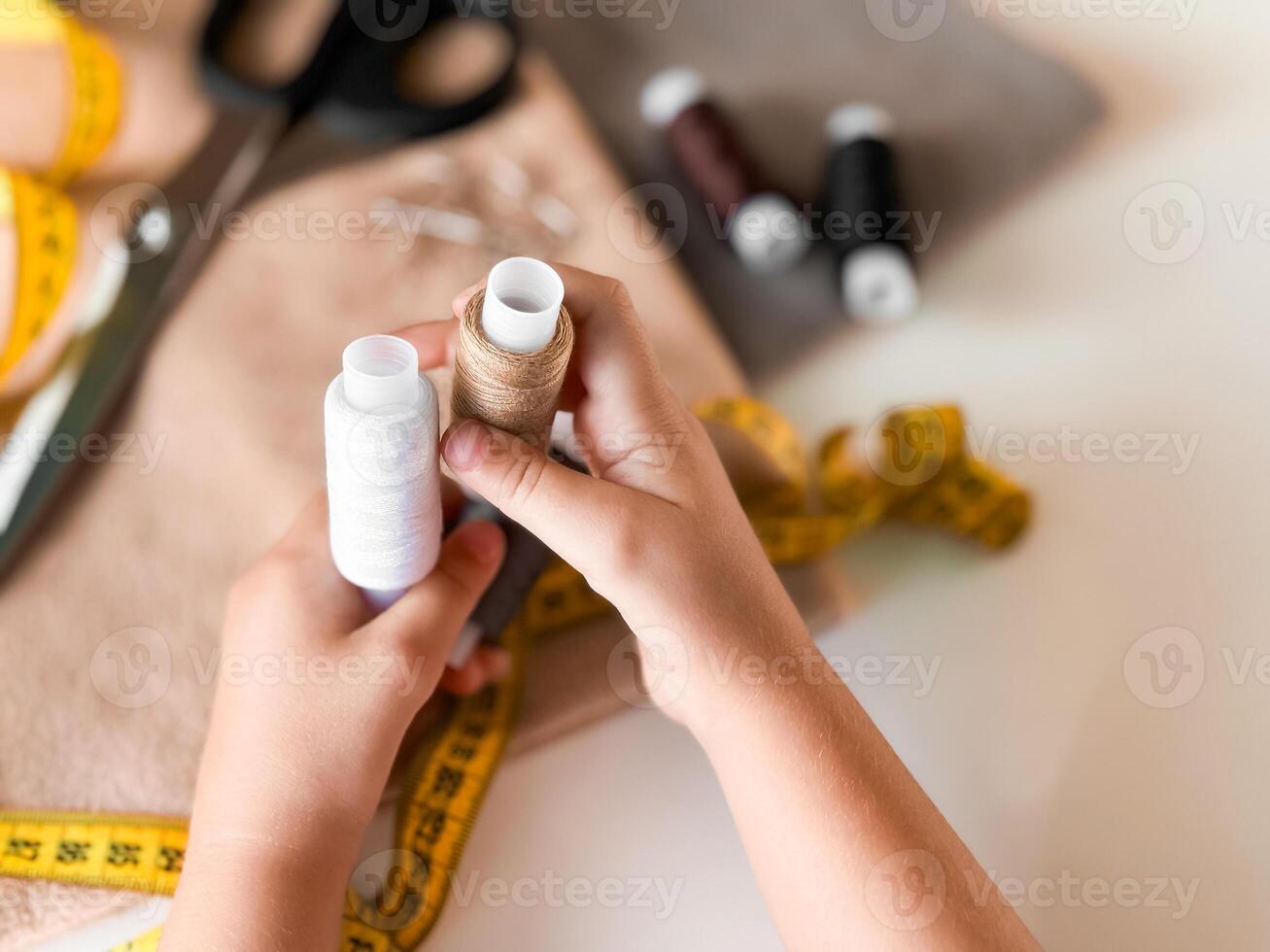 Hands holding thread spools for sewing with tape measure and fabric photo