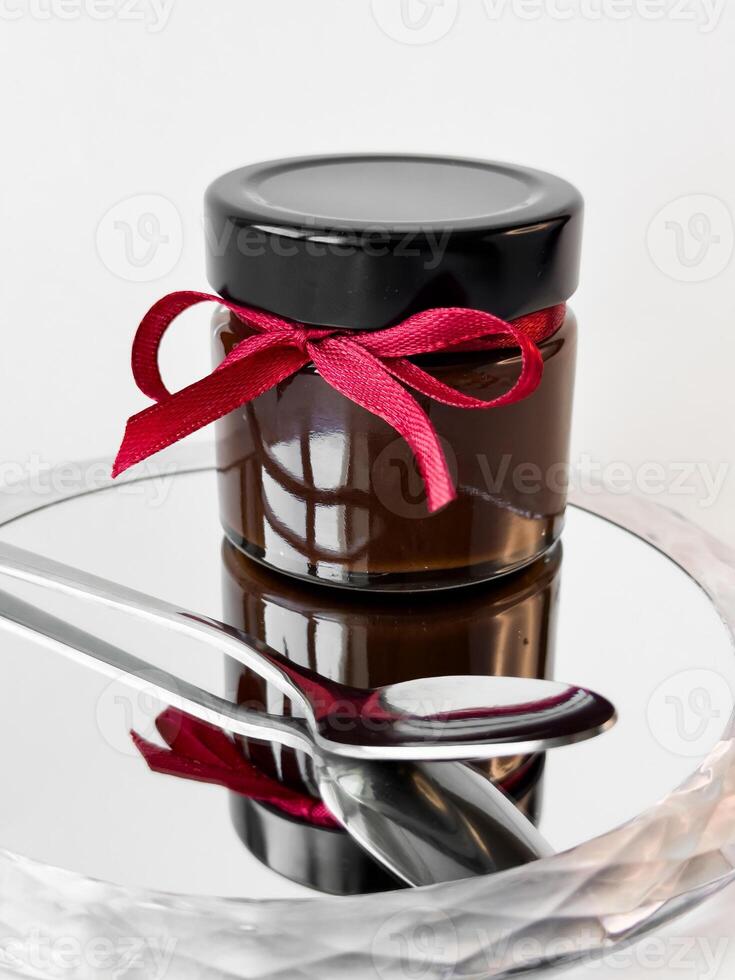 Elegant glass jar with red ribbon on mirrored surface photo