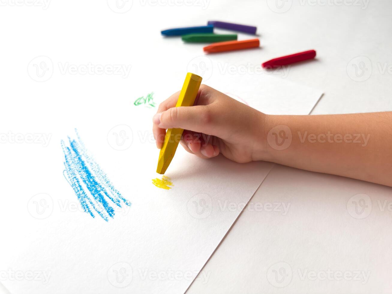 Childs hand drawing with colorful crayons on white paper photo