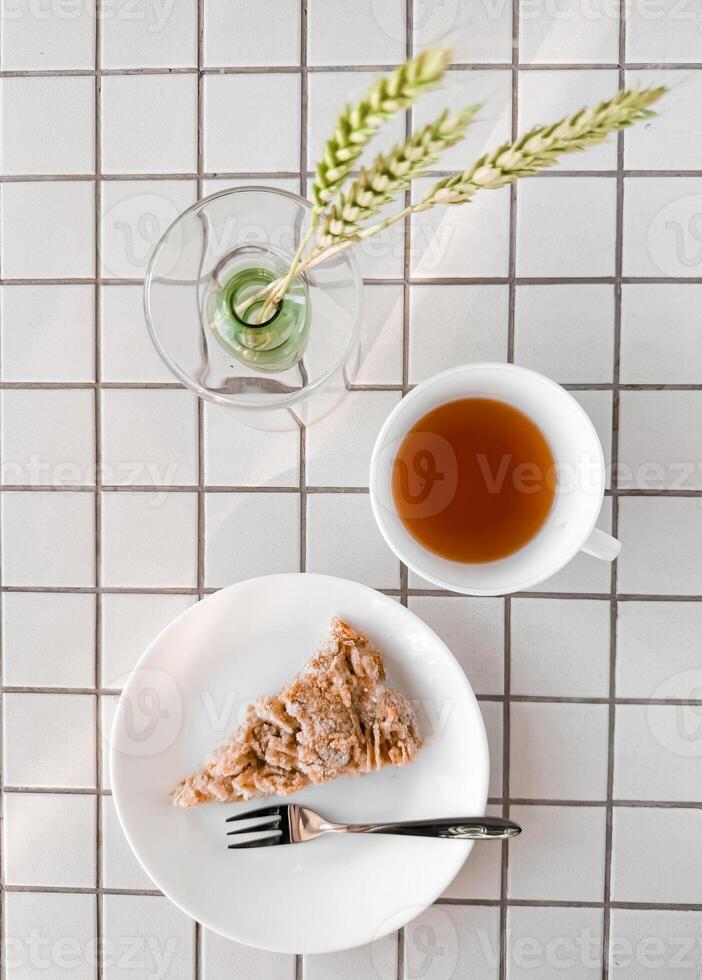 Breakfast pastry and tea on tiled table with vase and greenery photo