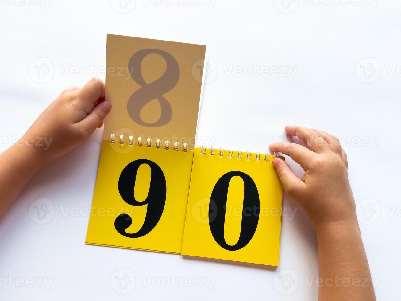 Childs hands flip through yellow pages with numbers. Displaying number 90 on white background photo
