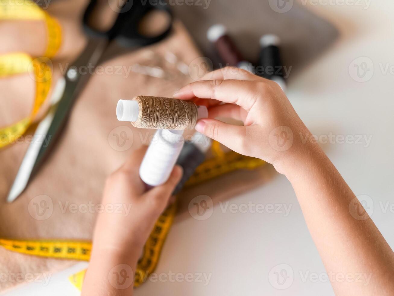 Hands winding thread for sewing crafts with scissors and fabric in background photo