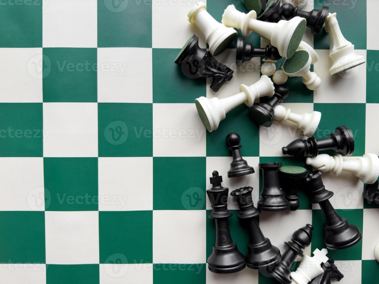 Chessboard and fallen chess pieces on green and white checkered board photo