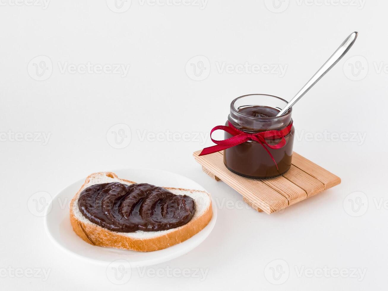 Delicious chocolate spread on bread with jar and red ribbon on white background photo