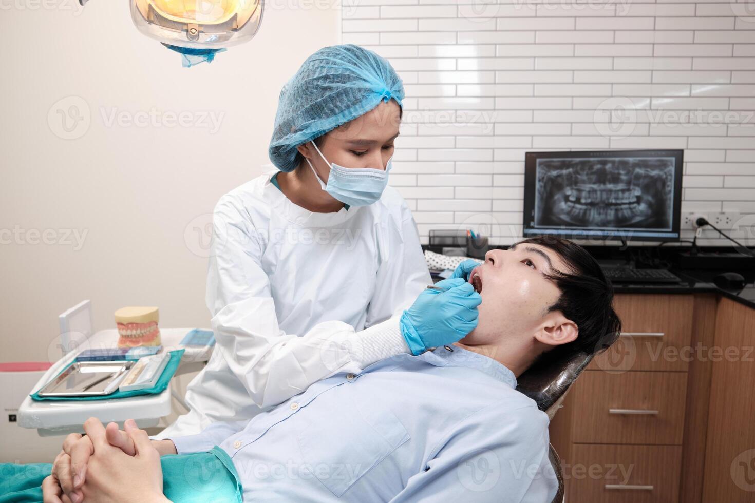 Asian female dentist examine young male patient teeth and toothache stomatology in dental clinic, well-being hygiene checks, and professional orthodontic healthcare work in doctor's office hospital. photo