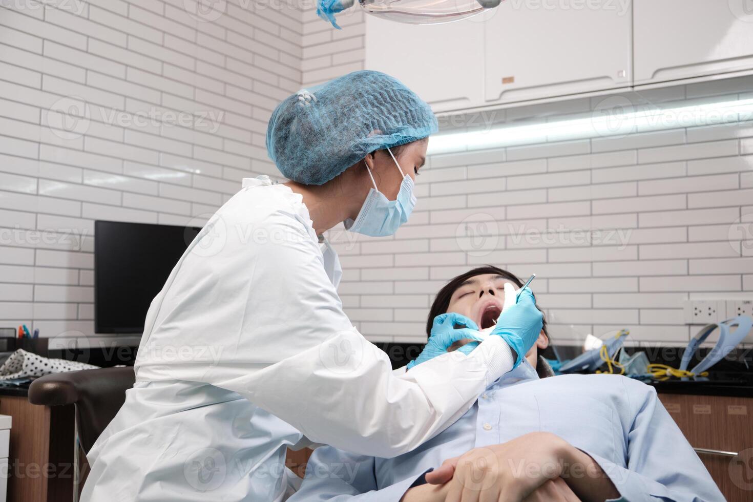 Asian female dentist examine young male patient teeth and toothache stomatology in dental clinic, well-being hygiene checks, and professional orthodontic healthcare work in doctor's office hospital. photo