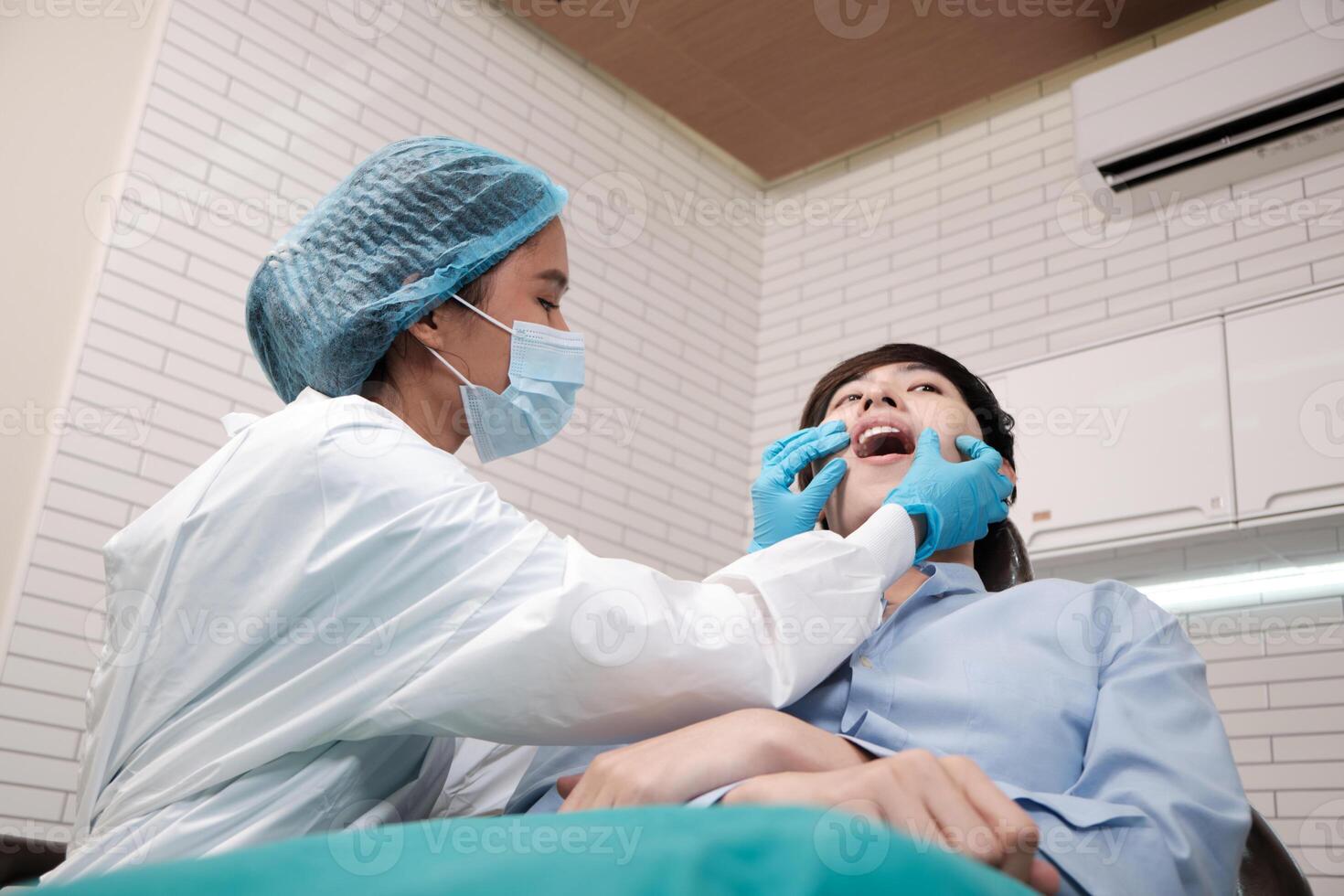 Asian female dentist examine young male patient teeth and toothache stomatology in dental clinic, well-being hygiene checks, and professional orthodontic healthcare work in doctor's office hospital. photo