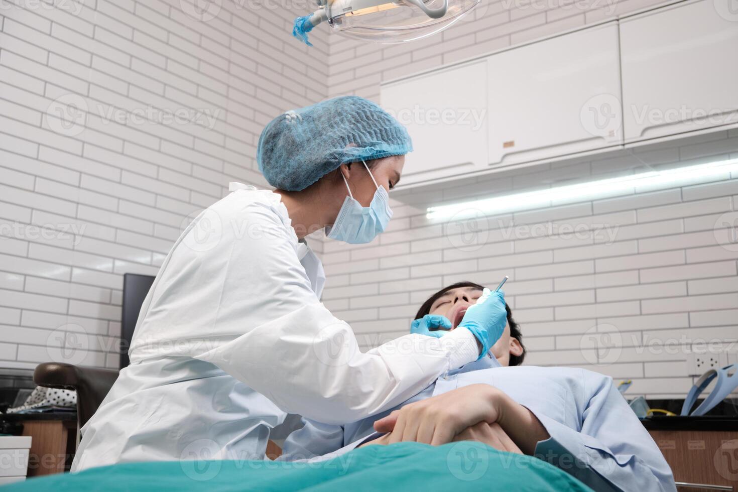 Asian female dentist examine young male patient teeth and toothache stomatology in dental clinic, well-being hygiene checks, and professional orthodontic healthcare work in doctor's office hospital. photo