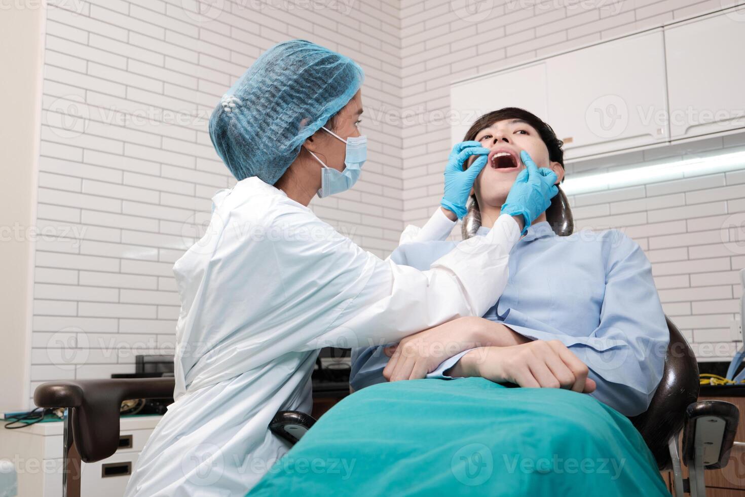 Asian female dentist examine young male patient teeth and toothache stomatology in dental clinic, well-being hygiene checks, and professional orthodontic healthcare work in doctor's office hospital. photo