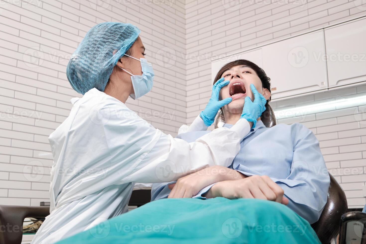 Asian female dentist examine young male patient teeth and toothache stomatology in dental clinic, well-being hygiene checks, and professional orthodontic healthcare work in doctor's office hospital. photo
