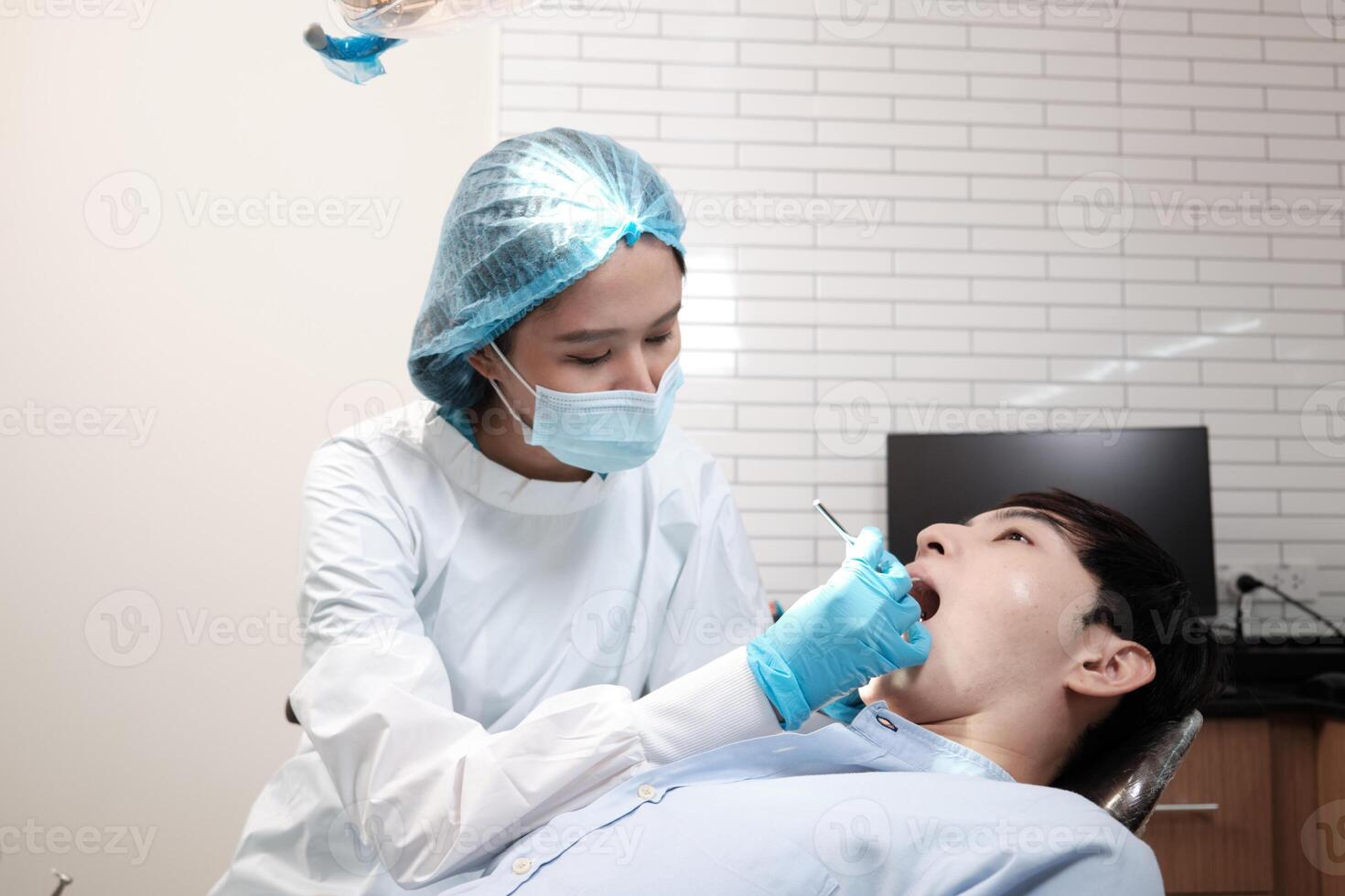 Asian female dentist examine young male patient teeth and toothache stomatology in dental clinic, well-being hygiene checks, and professional orthodontic healthcare work in doctor's office hospital. photo