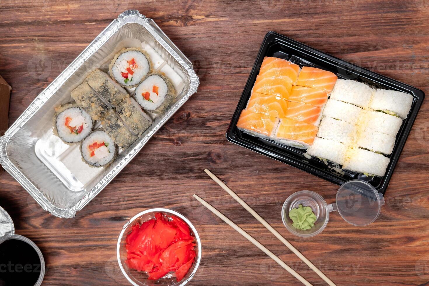 ordered food from an Asian cafe, fried rolls and tuna rolls, with ginger, soy sauce and wasabi in plastic packaging, on a wooden background photo