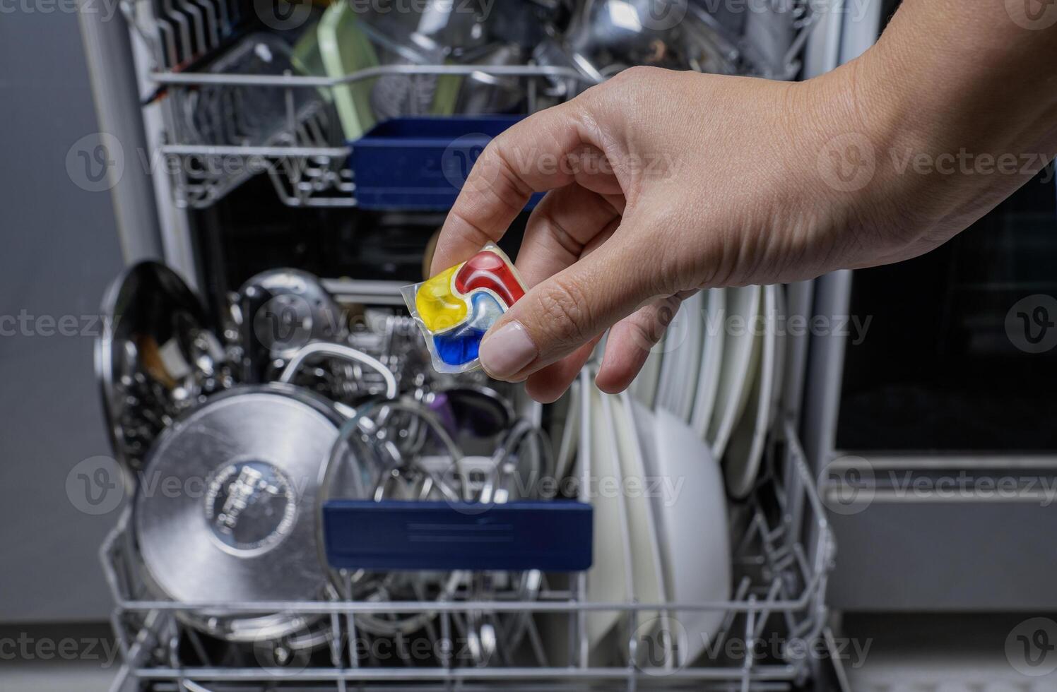 Woman putting detergen kapsul into open dishwasher photo