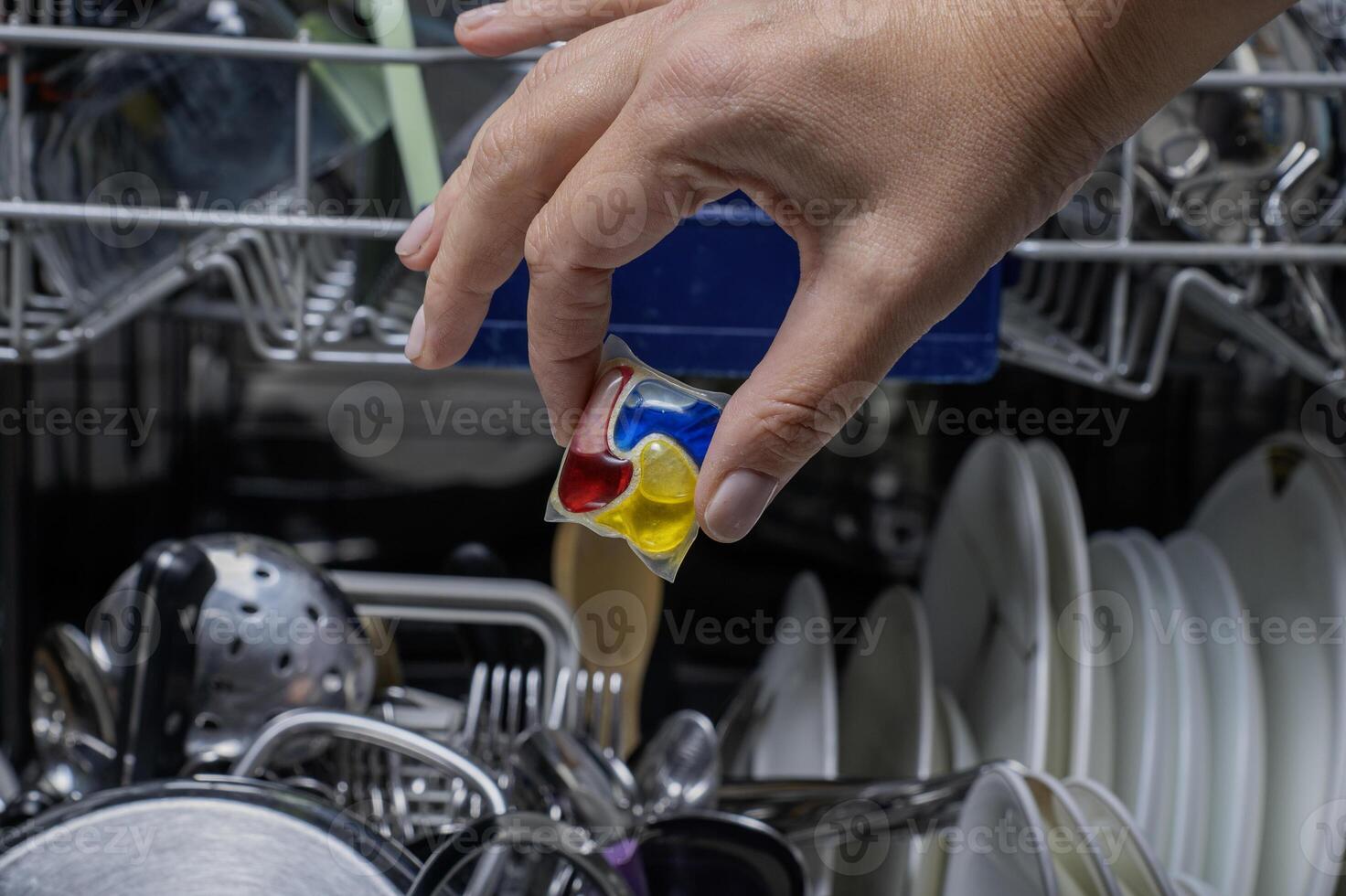 Woman putting detergen kapsul into open dishwasher photo