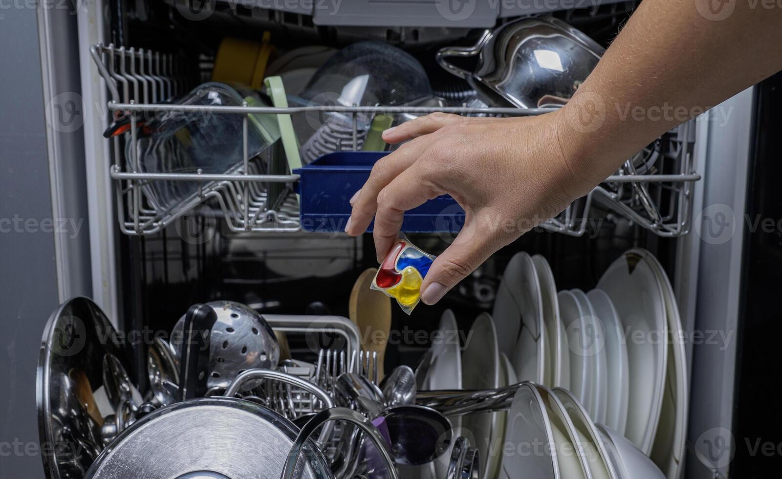 Woman putting detergen kapsul into open dishwasher photo