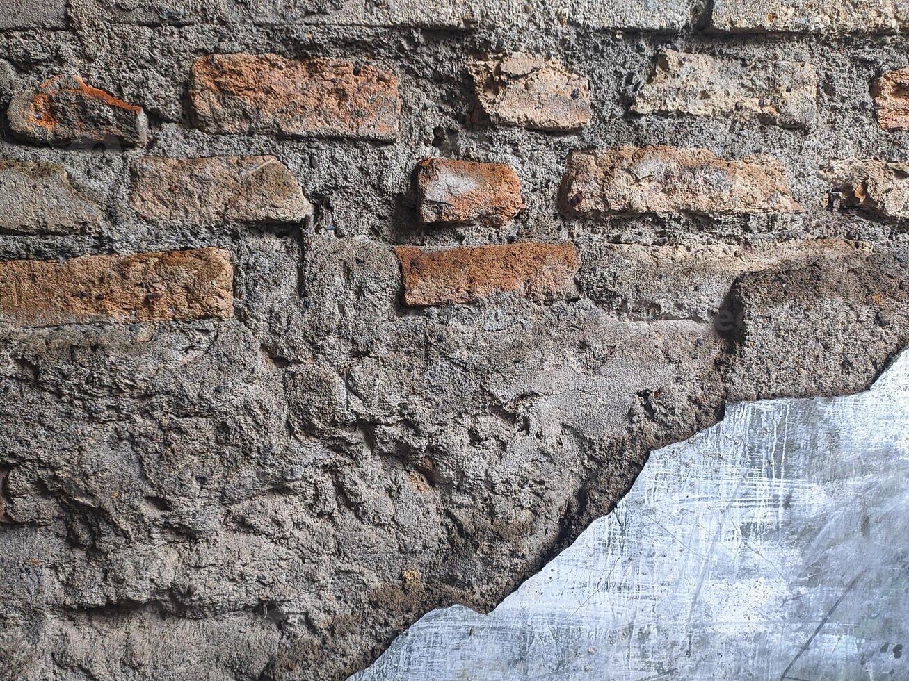 The fragments of an old brick wall have a reddish-orange texture, with gray cement plaster that has peeled off in the lower right corner. photo