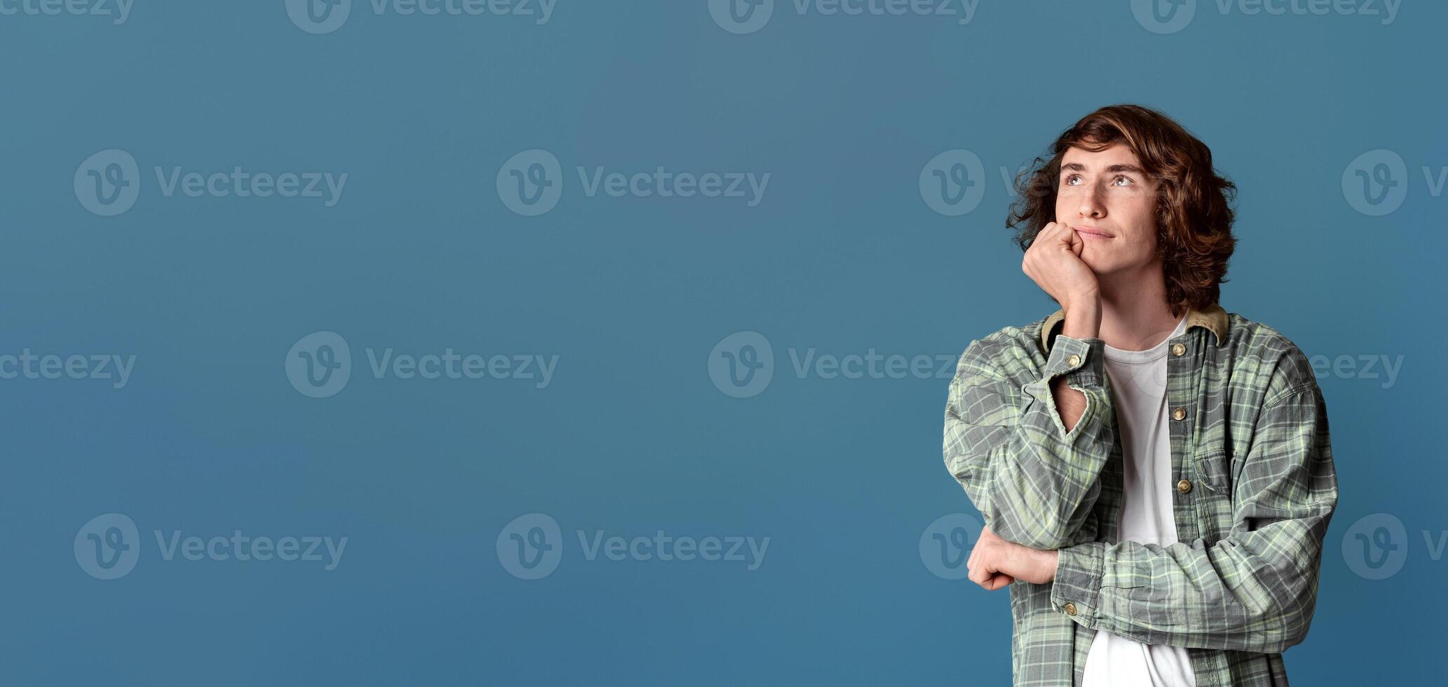 Charming teenage guy deep in thought on turquoise background photo