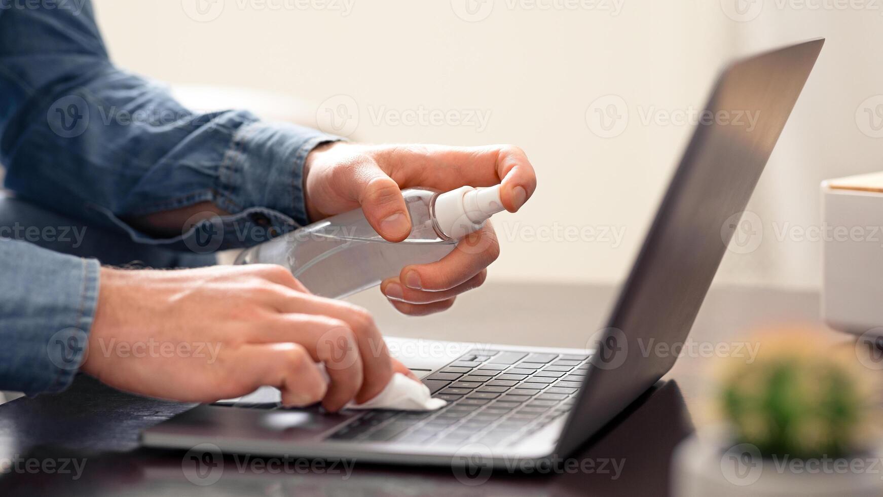 Electronics disinfection. Man cleaning laptop keyboard with sanitizer, close up photo