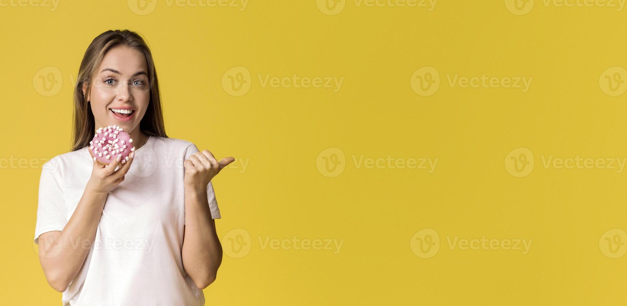 Tasty Sweets. Positive Millennial Lady Holding Donut And Pointing Aside At Copy Space On Yellow Background With Her Thumb Up, Panorama photo