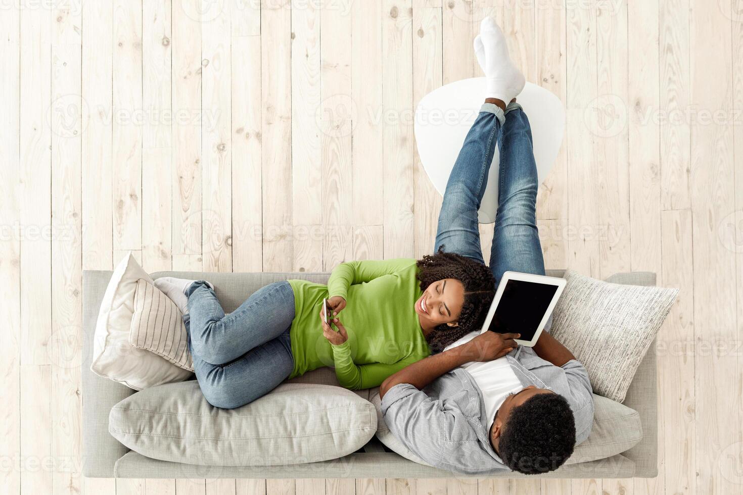 Weekend Leisure. Young Black Couple Relaxing On Couch With Digital Tablet And Smartphone, Top View With Copy Space photo