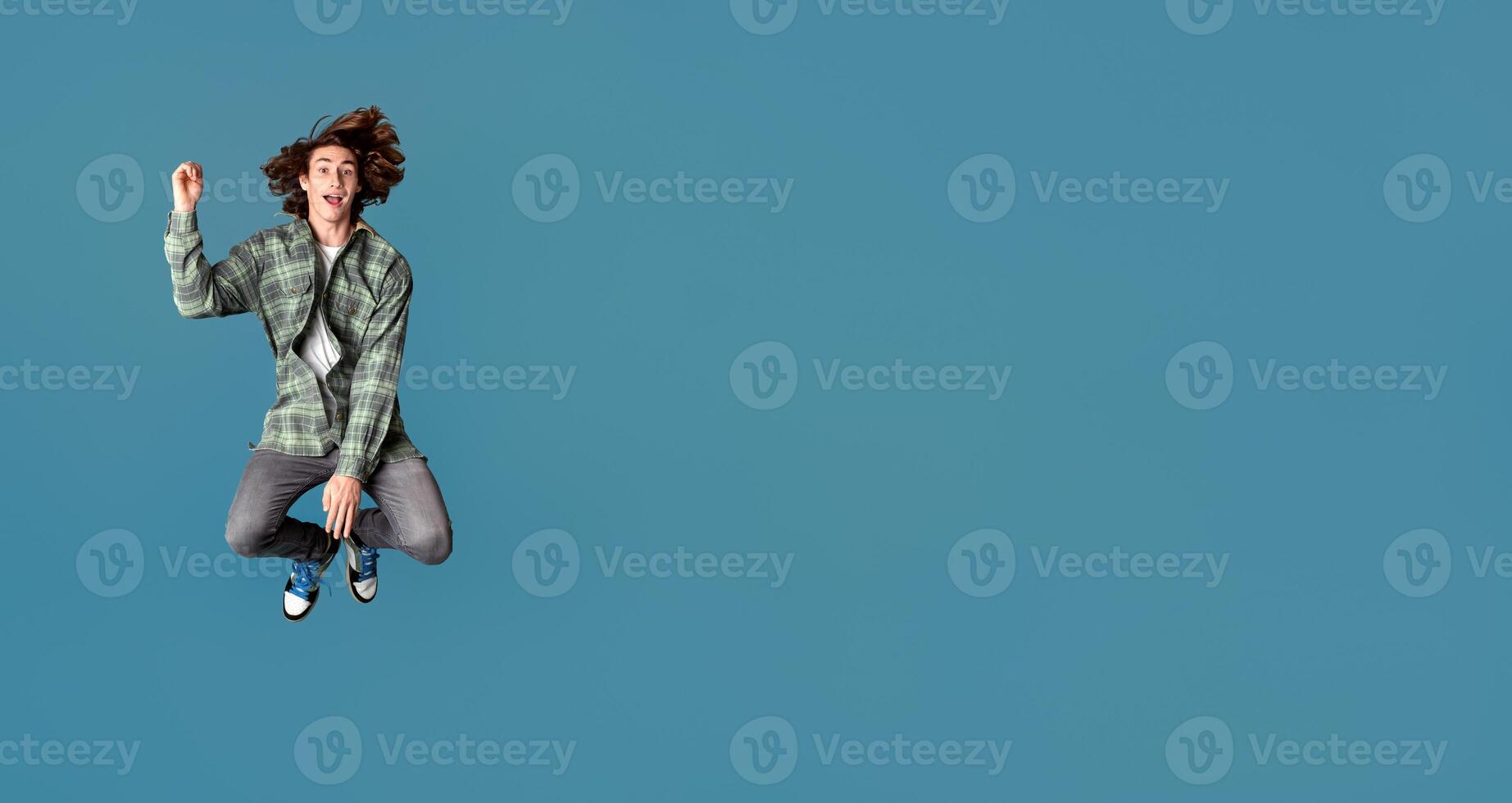 Happiness and freedom concept. Cheerful young guy in casual clothes jumping on turquoise background photo